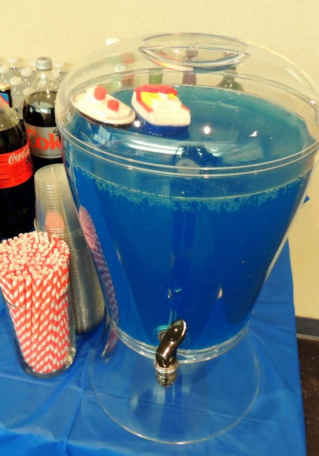 there is a blue liquid in the bowl with candy on it and two soda bottles next to it