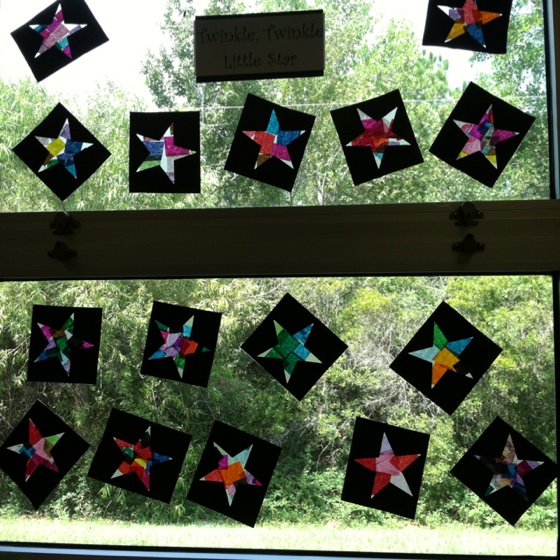 some paper stars are hanging on the window sill in front of trees and bushes