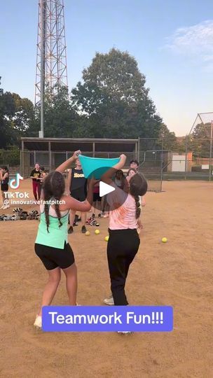 two girls are holding up their hats in the middle of a softball field with other people behind them