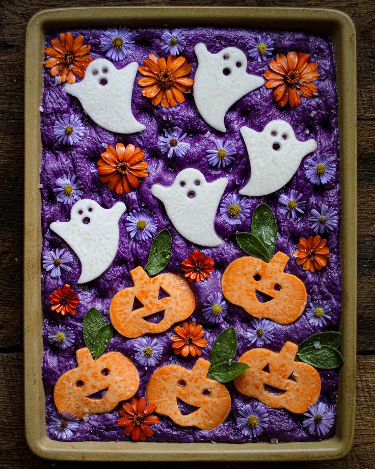 decorated cookies in the shape of ghost and pumpkins on a purple background with daisies