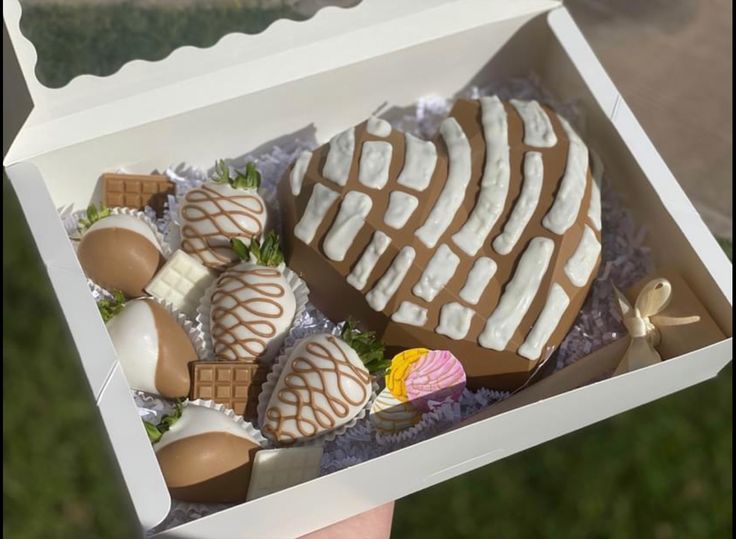 a person is holding a box with chocolates and strawberries in it on the grass