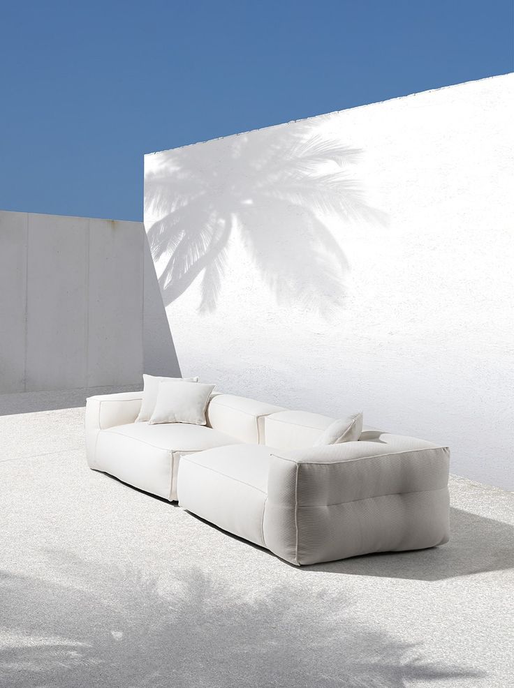 a white couch sitting on top of a cement floor next to a wall with a palm tree