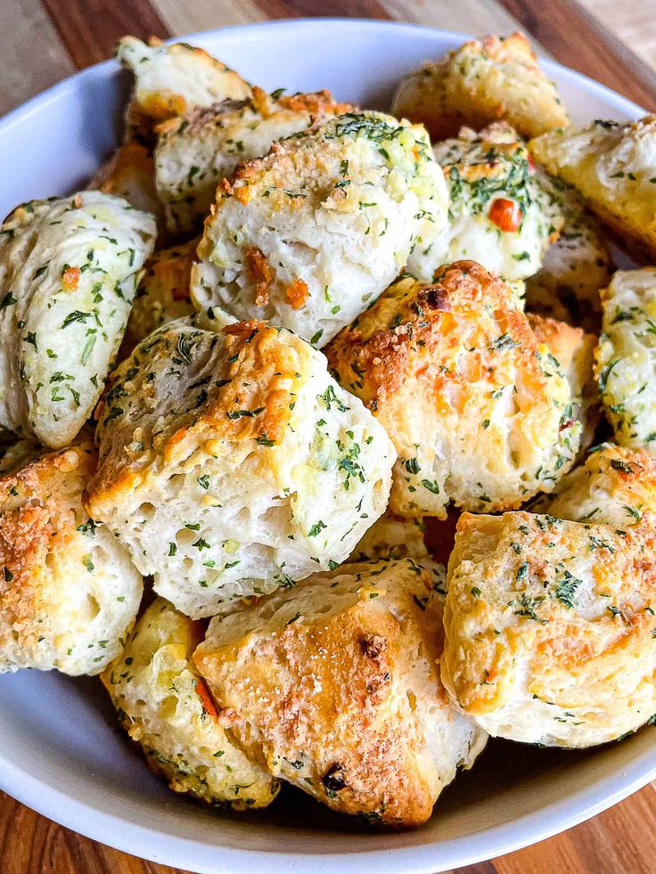 a white bowl filled with cheesy biscuits on top of a wooden table