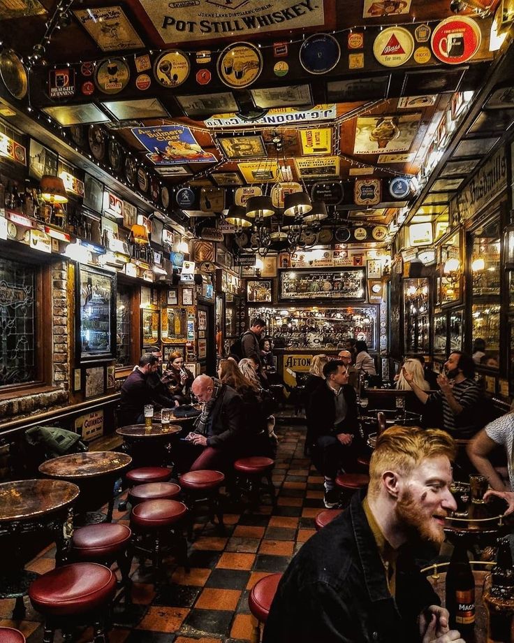 people sitting at tables in a bar with lots of beer bottles on the walls and ceiling