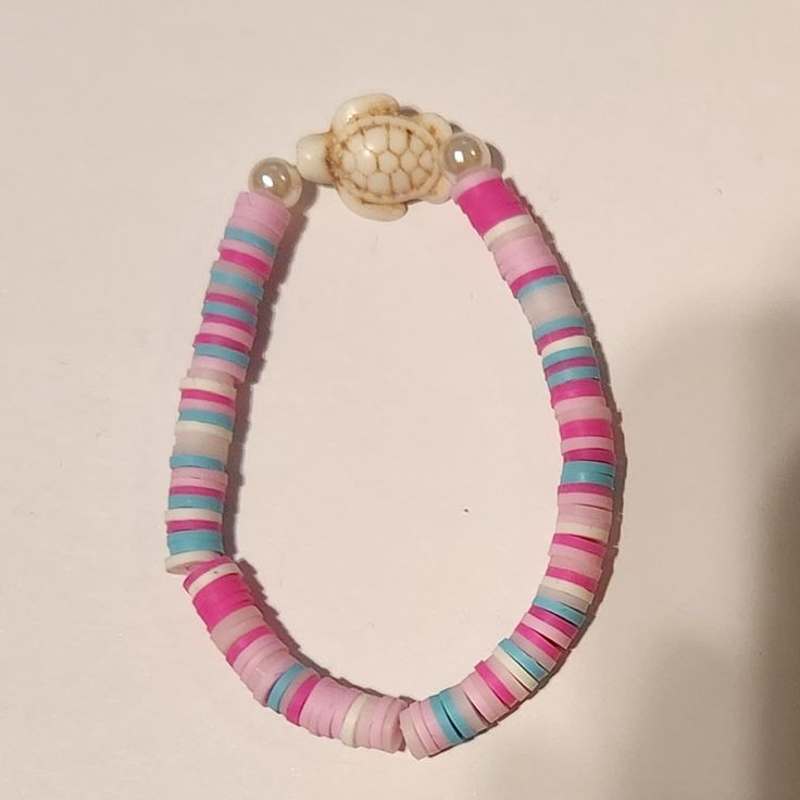 a pink, blue and white beaded bracelet with a shell on the end is hanging from a hook