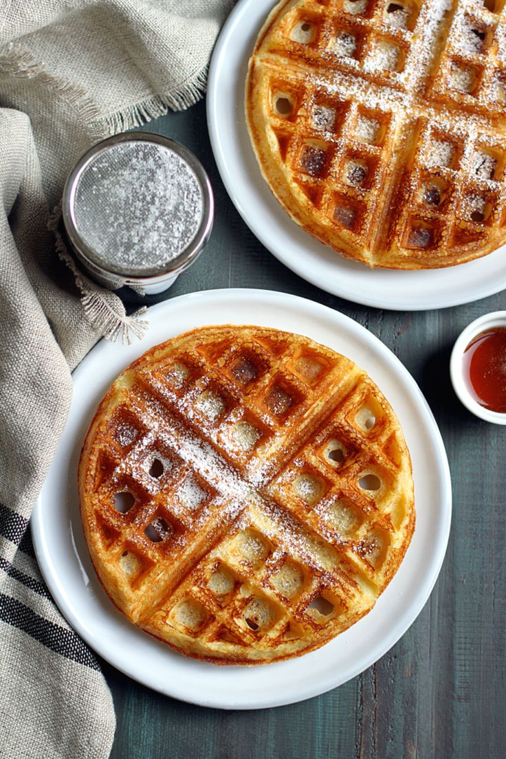 two waffles sitting on top of white plates covered in powdered sugar and syrup