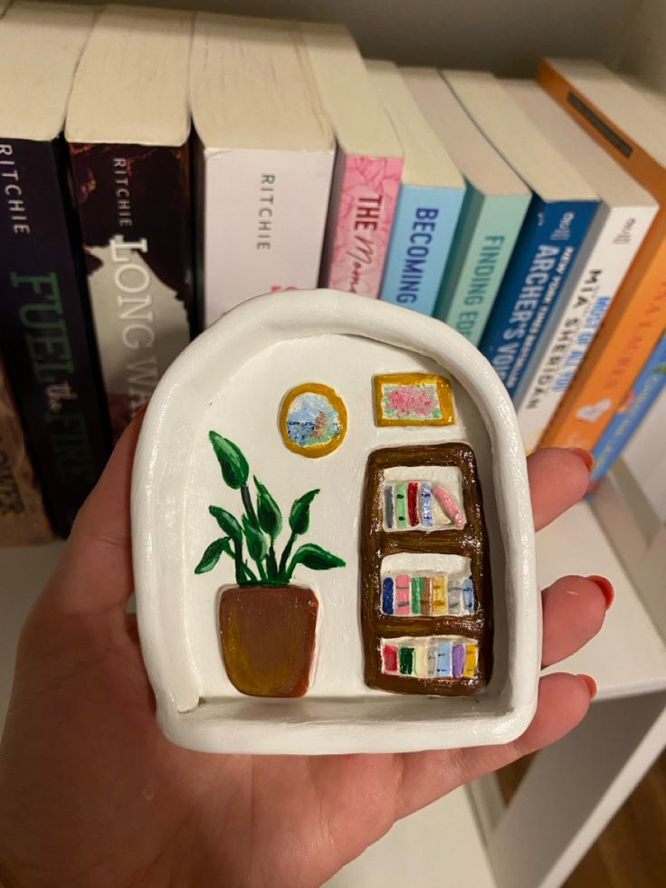 a hand holding a small white plate with sushi and plants on it in front of bookshelves