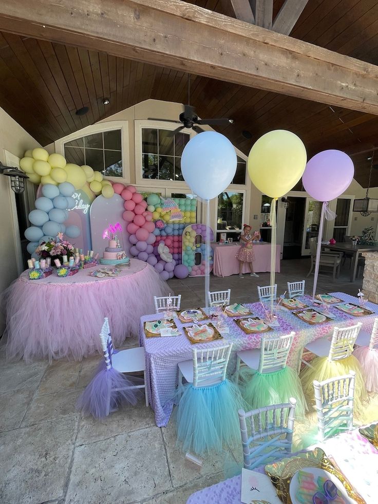 an outdoor party with balloons, cake and other items on the table in pastel colors