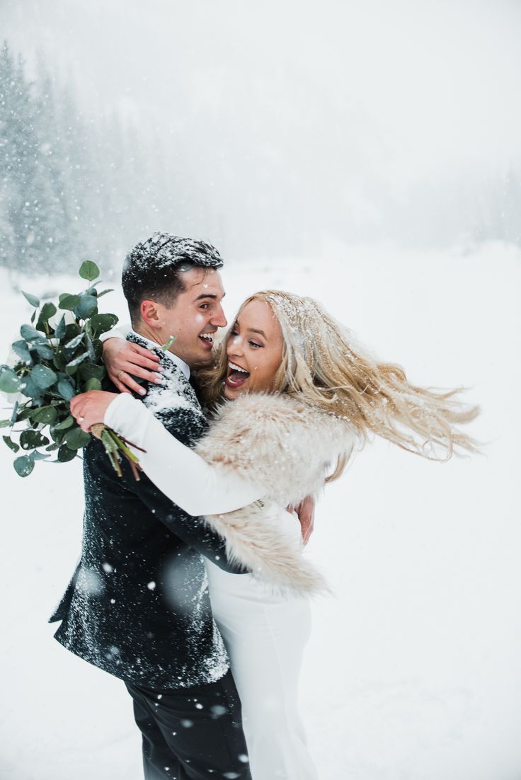 a man and woman are hugging in the snow with one holding a bouquet of flowers