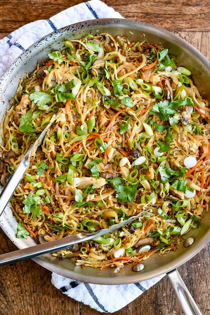 a pan filled with noodles and vegetables on top of a wooden table next to utensils