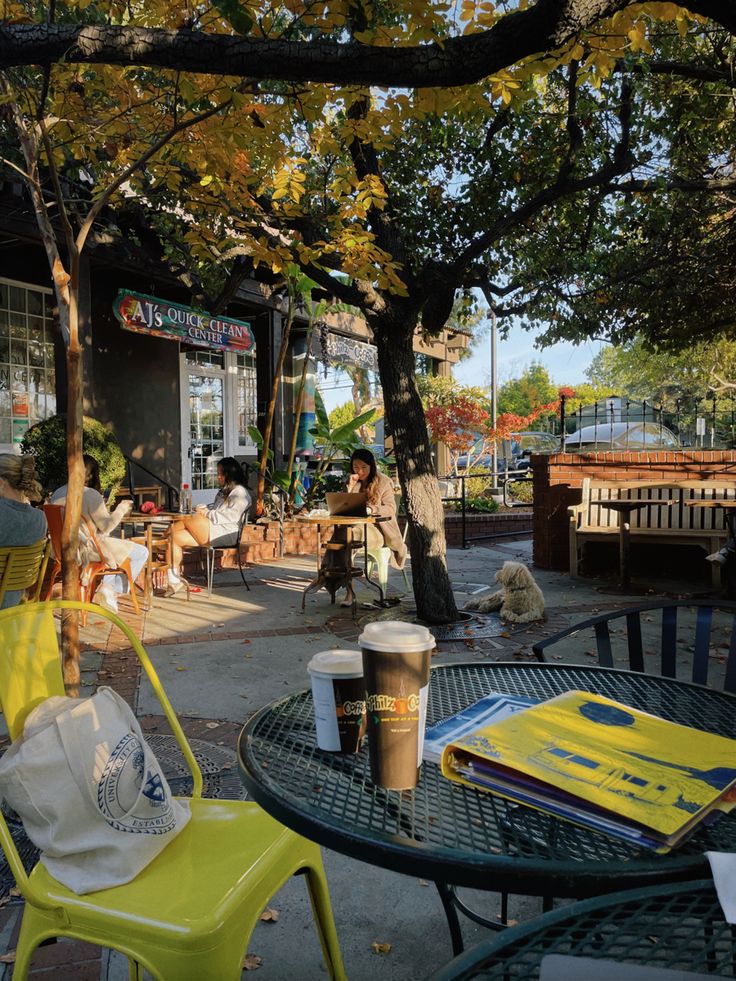 people are sitting at tables outside in the shade