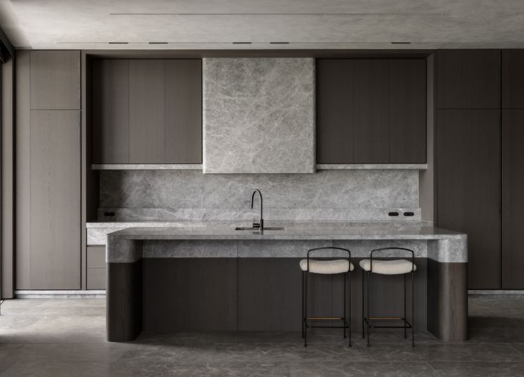 two stools sit in front of an island with marble counter tops and cabinets on either side