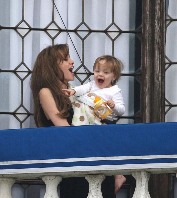 a woman holding a baby on top of a balcony next to a blue and white bench