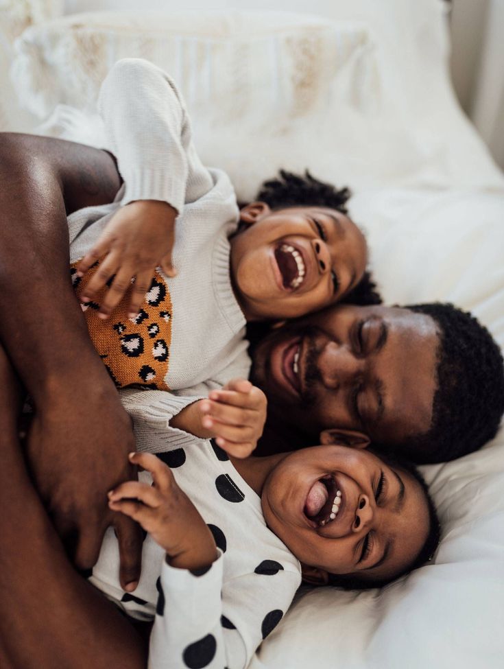 an adult and child laying on top of each other in the bed smiling at the camera