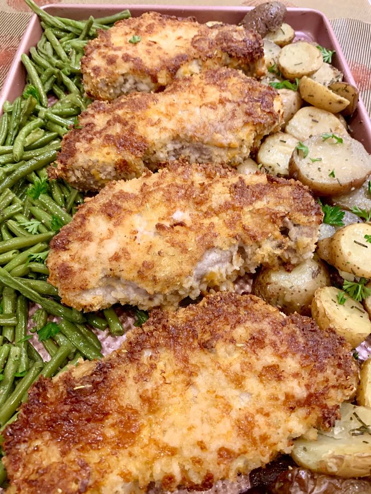 two pieces of chicken with potatoes and green beans in a pink tray on a table