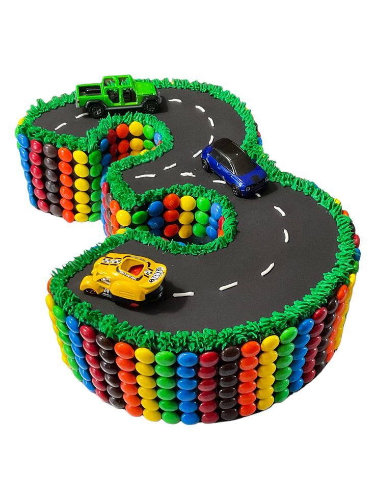 a cake shaped like the number five with cars on it and rainbow colored icing