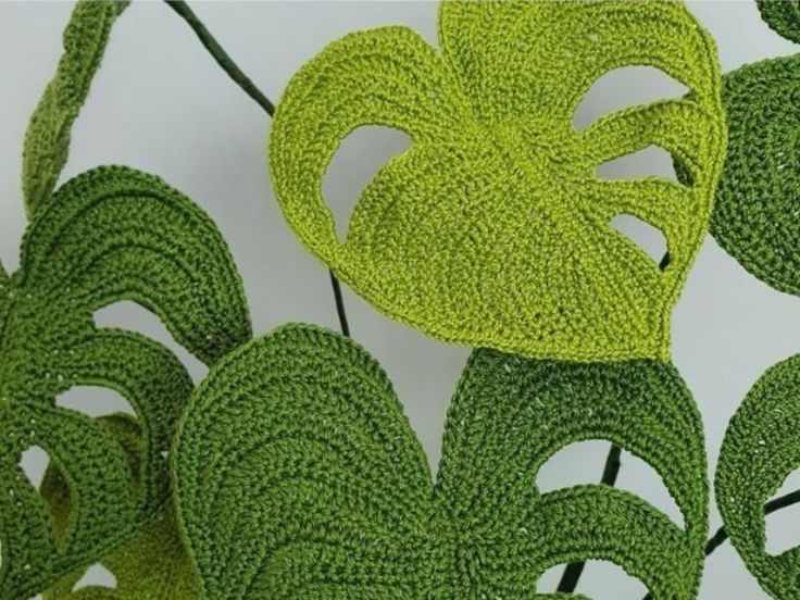 green crocheted leaves are arranged on a white surface, with one large leaf in the center