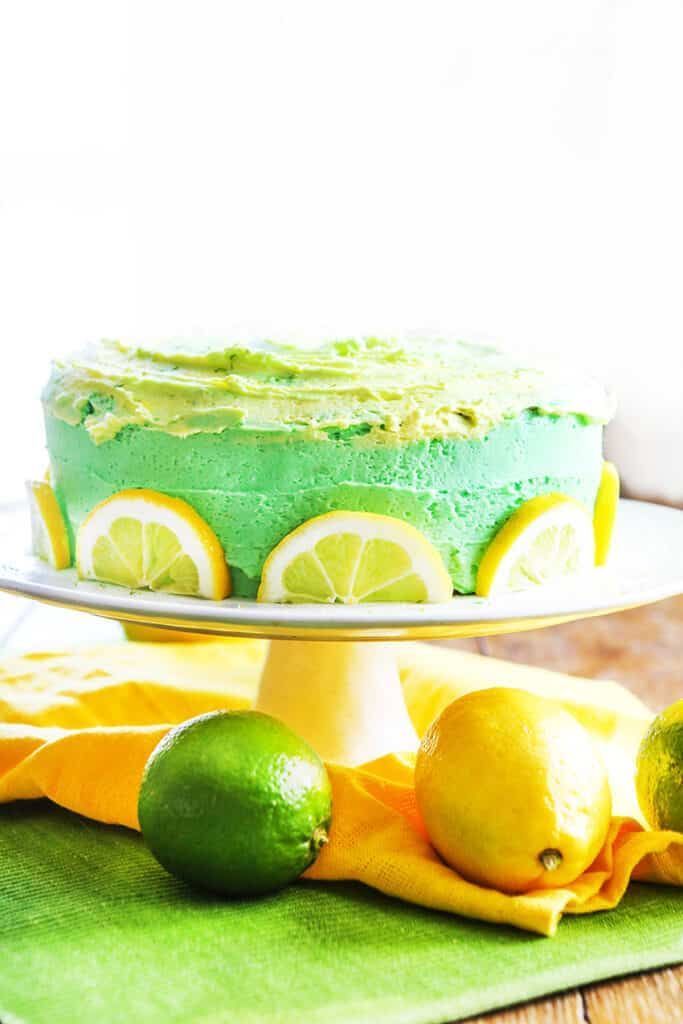 a green cake with lemons and limes on the side, sitting on a table