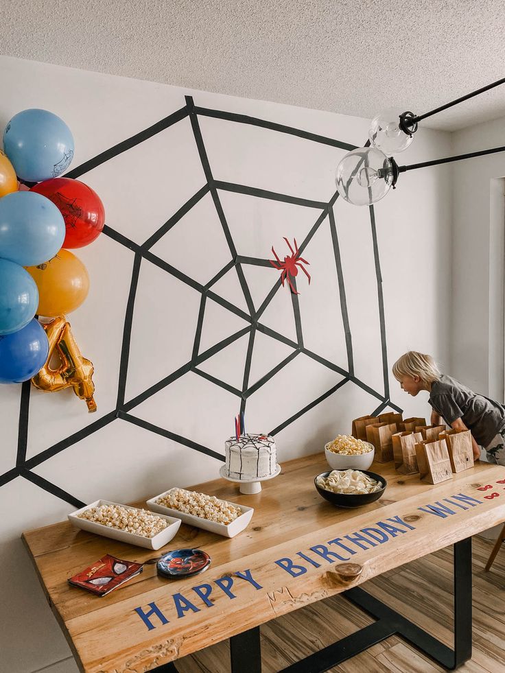 a birthday party with balloons and cake on a table in front of a spider web wall