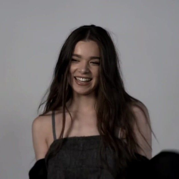 a woman with long brown hair smiling and wearing a black top in front of a gray background