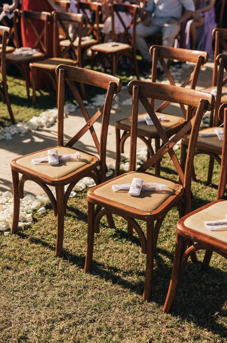 rows of wooden chairs with napkins on them sitting in the grass next to each other