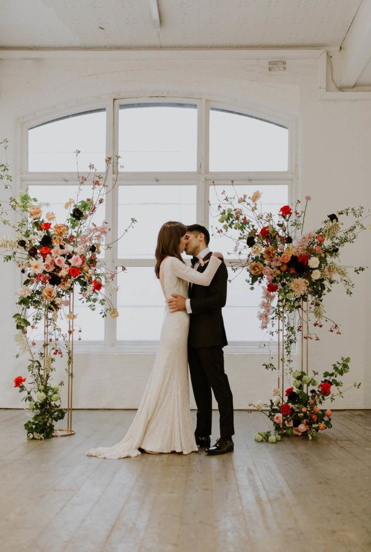 a bride and groom kissing in front of an arch with flowers