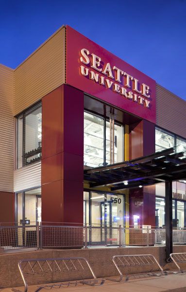 the entrance to seattle university is lit up at night, with benches in front of it