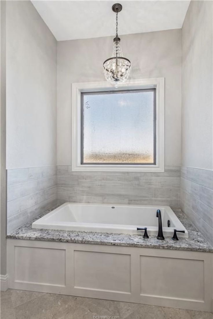 a bath tub sitting under a window next to a chandelier in a bathroom