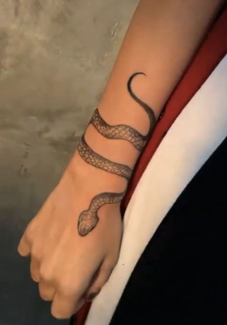 a woman's arm with a snake tattoo on her left wrist and the other hand