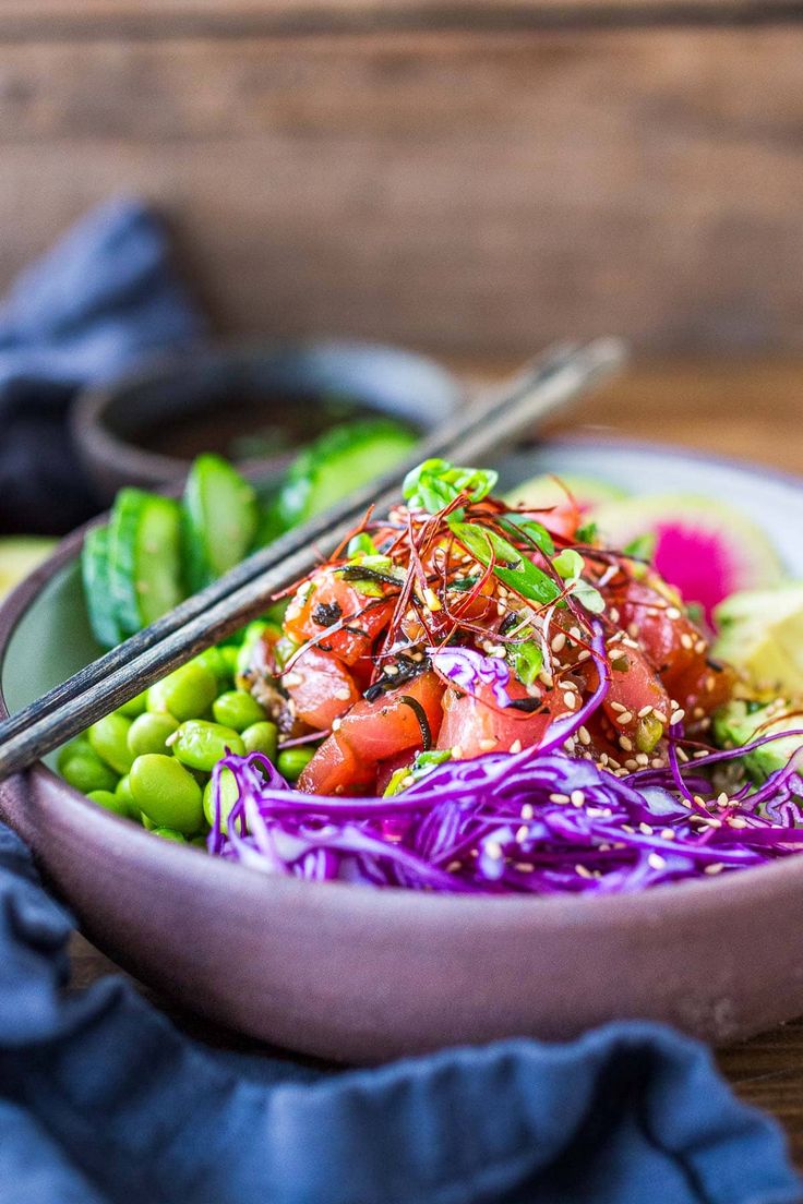 a bowl filled with vegetables and chopsticks on top of a wooden table next to a blue napkin