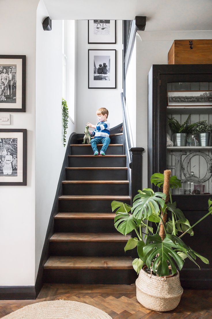 a young boy sitting on top of a stair case next to a potted plant