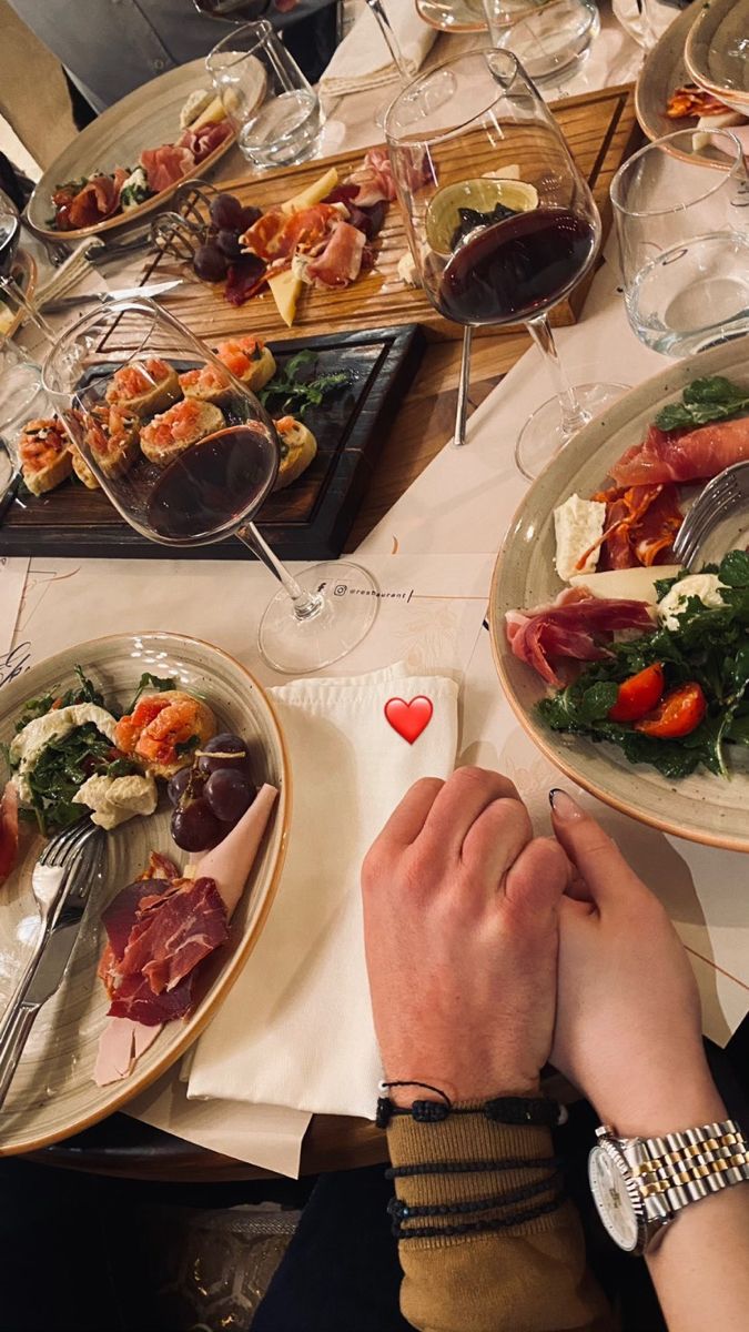 two people are sitting at a table with plates of food and wine glasses on it