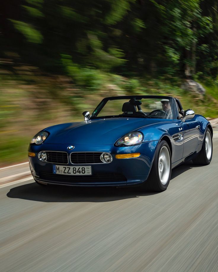 a blue sports car driving down the road with trees in the backgrouund