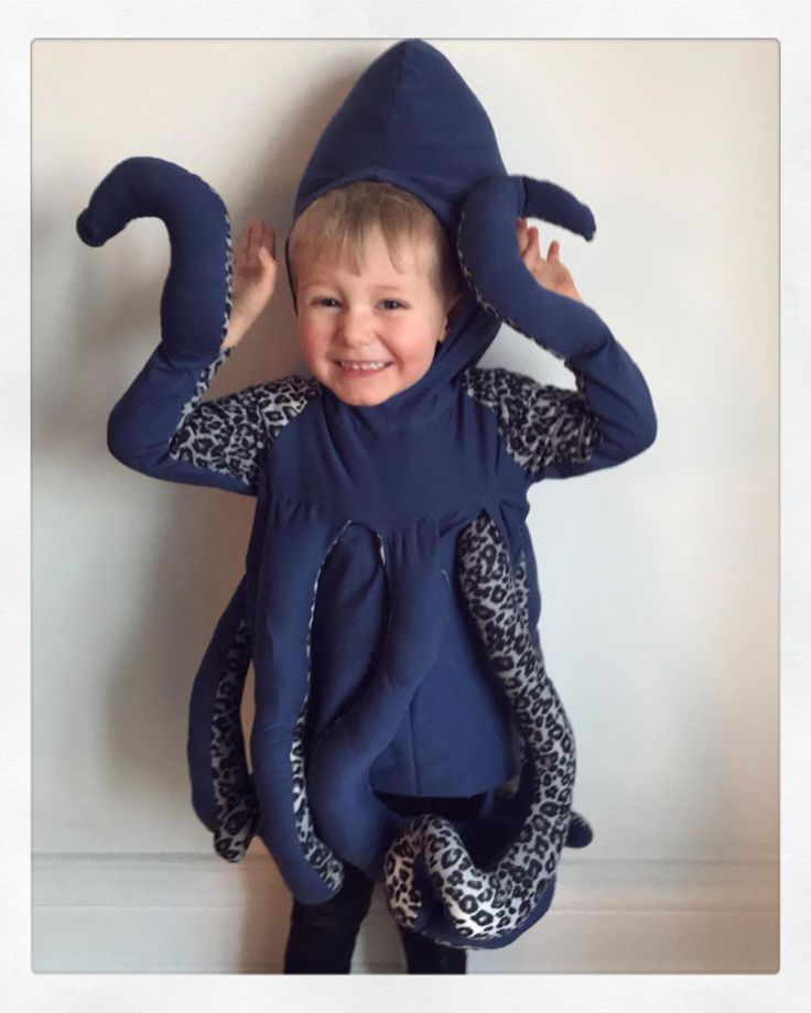 a young boy wearing an octopus costume standing in front of a wall with his hands on his head