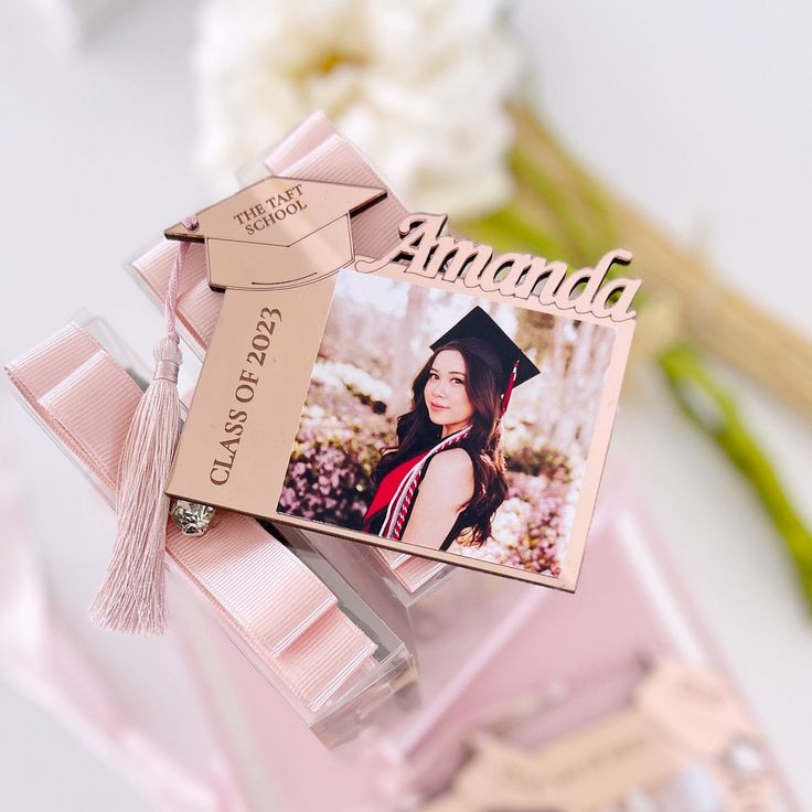 a graduation card with a pink ribbon attached to it and a flower in the background