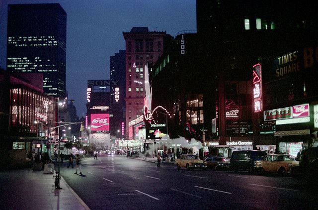 an empty city street at night with tall buildings and neon signs on the sides of it