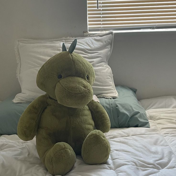 a green stuffed animal sitting on top of a bed