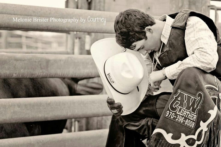 black and white photograph of a man wearing a cowboy hat leaning on a fence with his face close to the ground