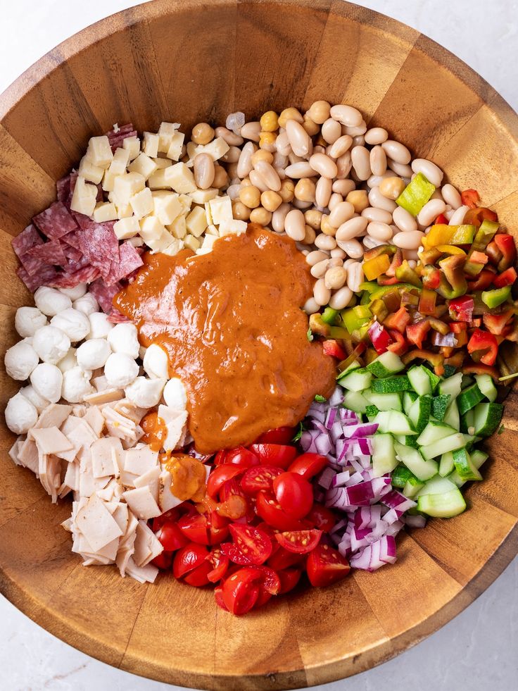 a wooden bowl filled with different types of vegetables and sauce on top of each other