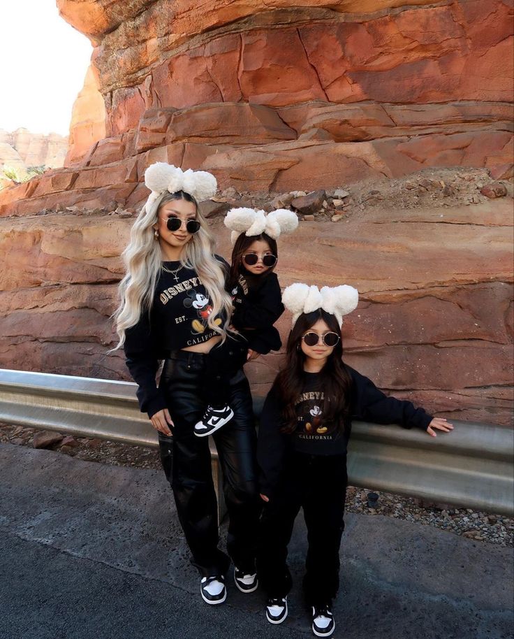 three girls in matching outfits standing next to a rock formation with their arms out and one girl wearing sunglasses on her head