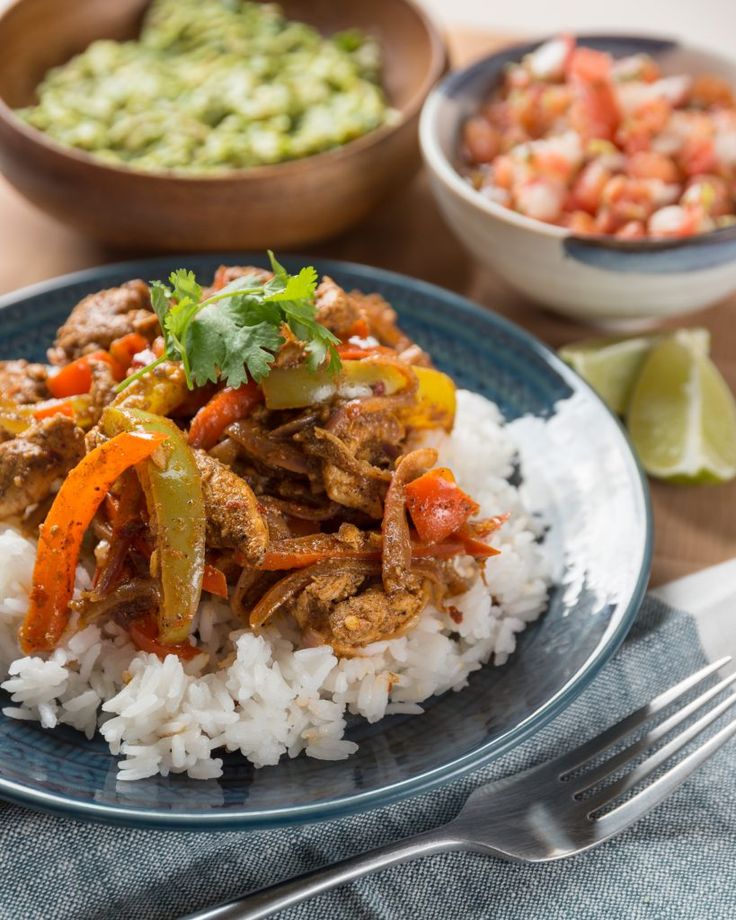 a blue plate topped with rice covered in meat and veggies next to a bowl of guacamole