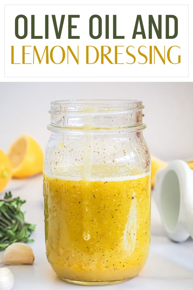 a jar filled with lemon dressing sitting on top of a table next to garlic and herbs