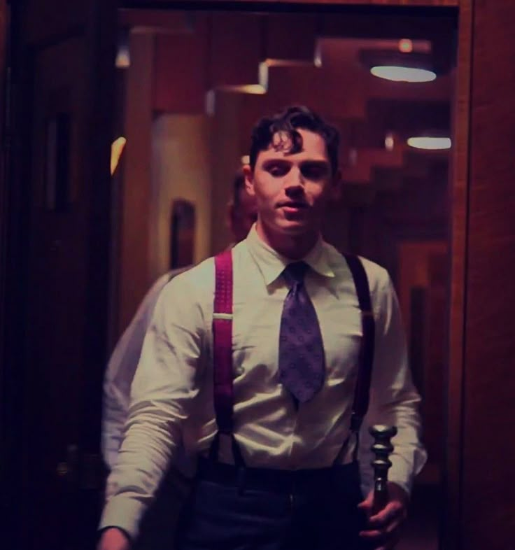 a man wearing suspenders and a tie standing in front of a mirror