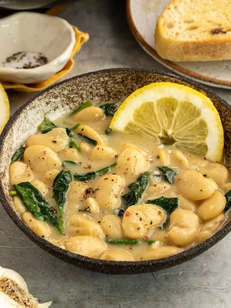 a bowl filled with pasta and spinach next to slices of lemon on a table