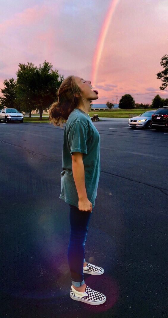 a person standing in the middle of a parking lot with a rainbow in the background