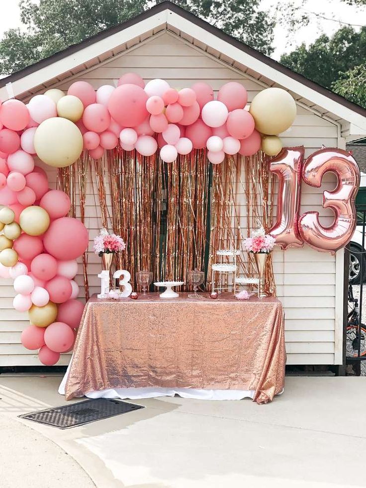 a table topped with pink, gold and white balloons next to a large number 13 sign