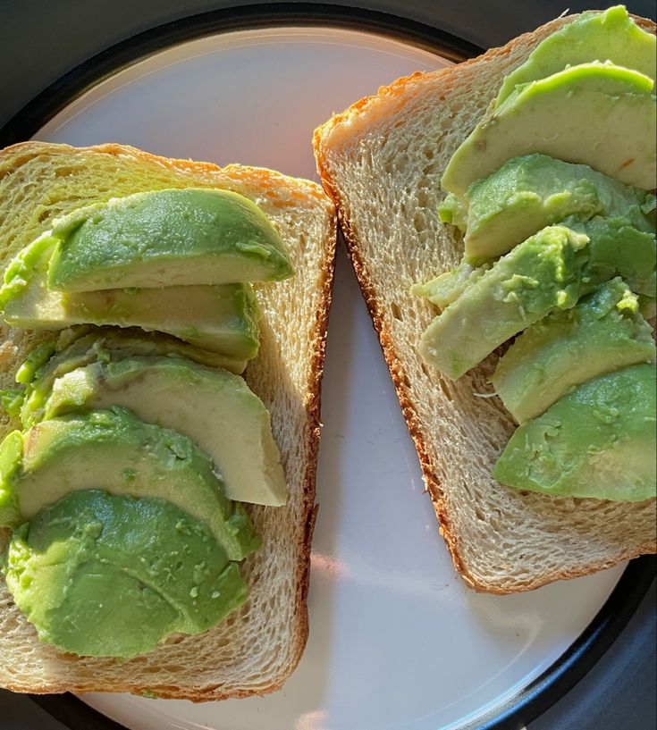 two pieces of bread with avocado spread on them sitting on a white plate