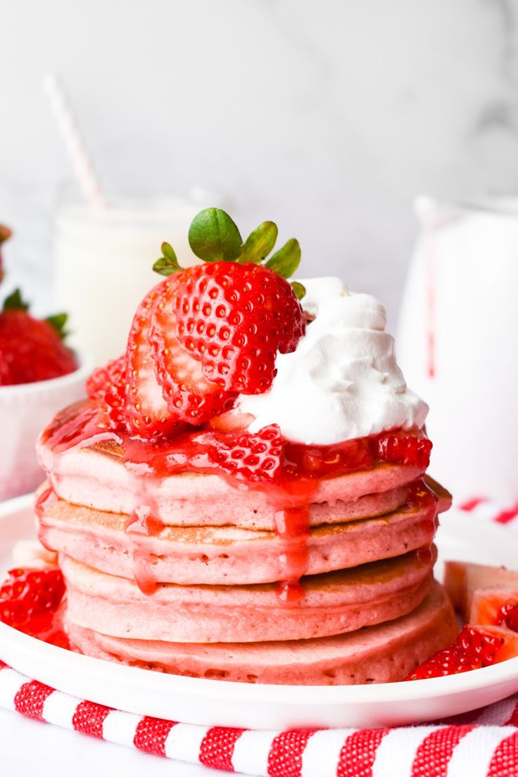 a stack of pancakes topped with whipped cream and strawberries