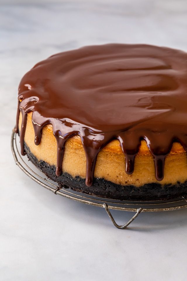 a cake with chocolate icing sitting on top of a metal rack in front of a marble counter