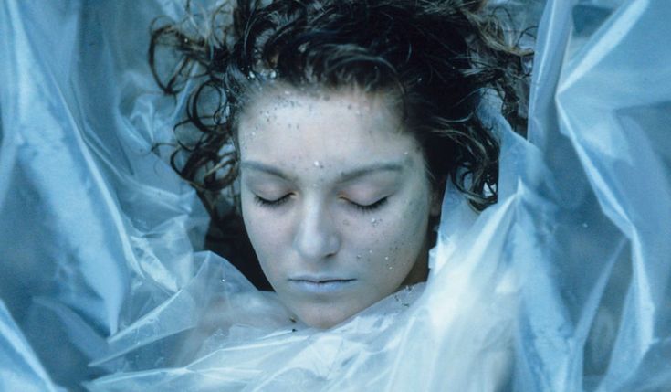 a woman with her eyes closed laying down in a white sheeted area, covered by plastic